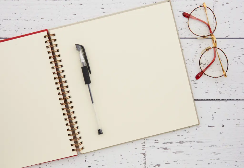 A notebook lying open on a pale table, with a pen and a pair of glasses