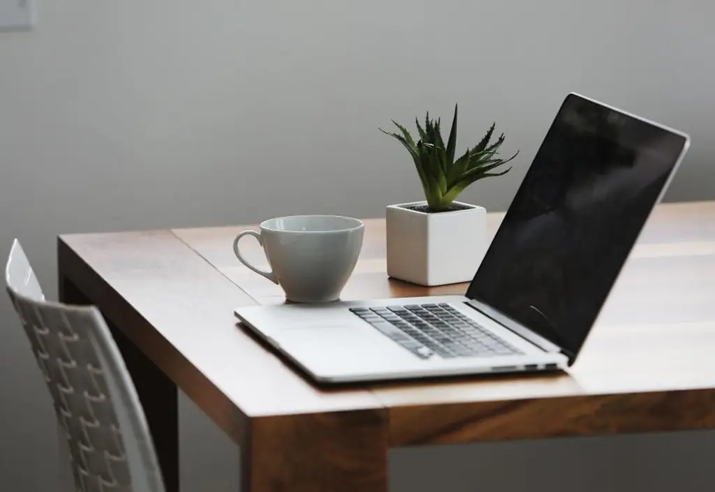 A laptop on a kitchen table showing a video call, next to a notebook and a bowl of cereal